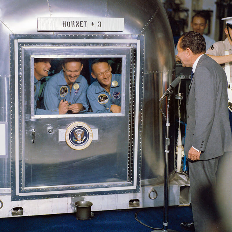 Neil Armstrong, Michael Collins e Edwin “Buzz” Aldrin, em quarentena, conversam com Richard Nixon