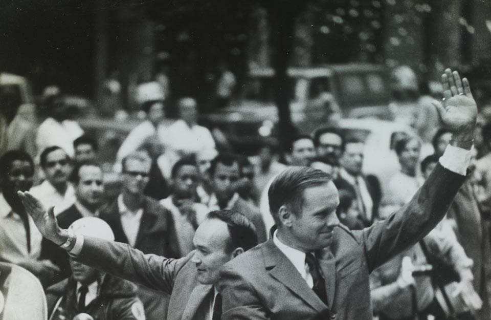 Michael Collins e Neil Armstrong acenam durante passeio de carro aberto